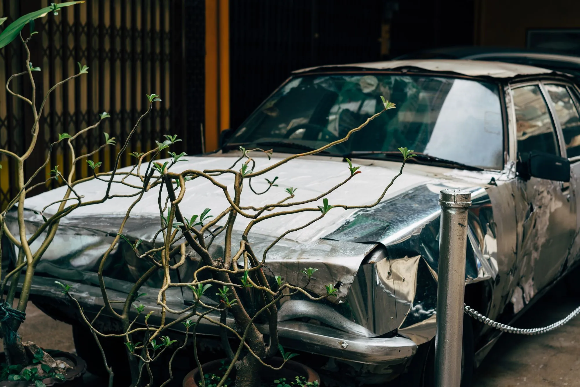 A silver sedan with a crushed hood and broken grille parked beside a curb.