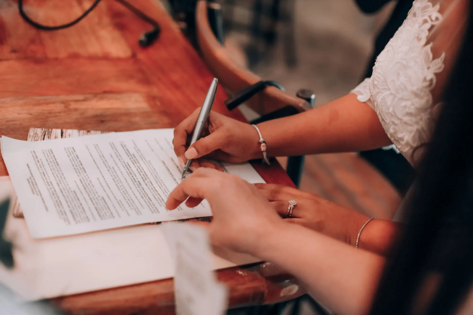 Two people signing documents at a wooden table.